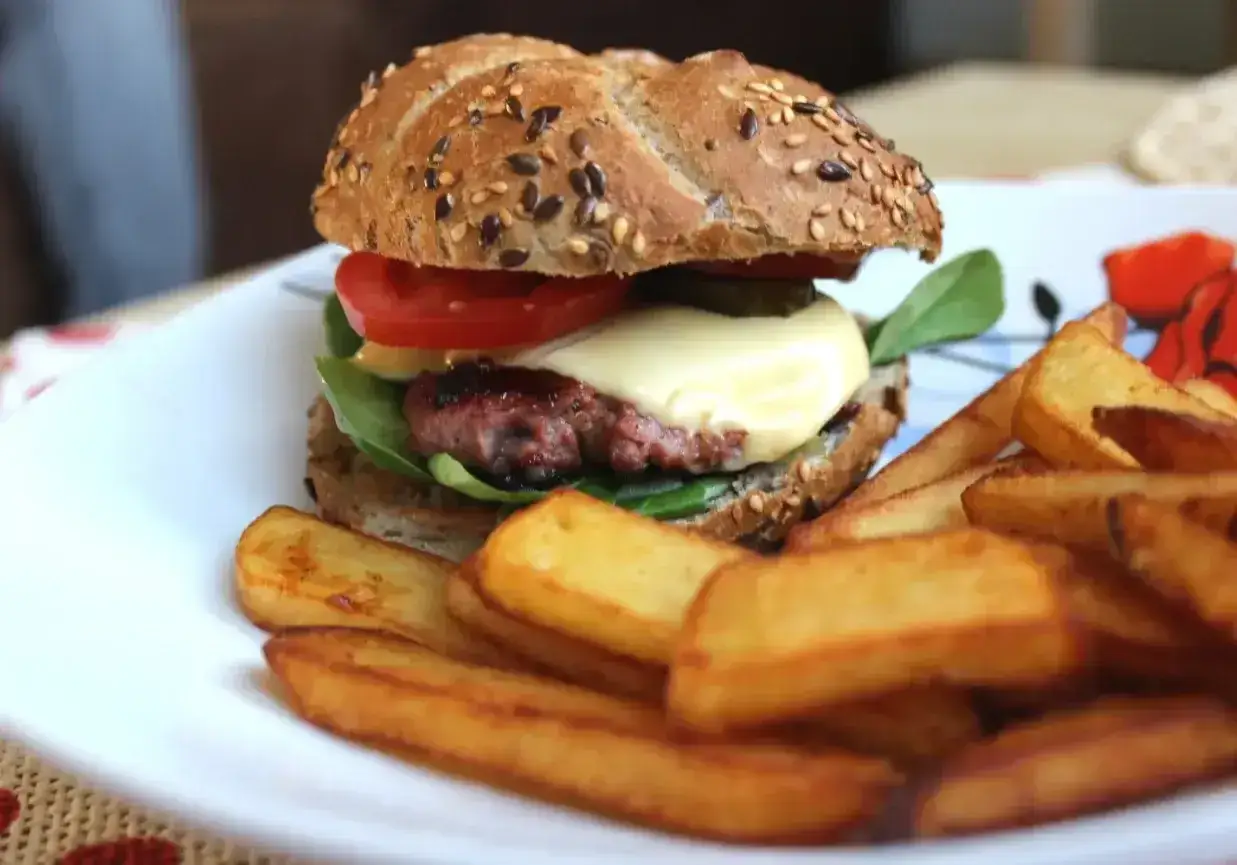 Pyszny, domowy małomiasteczkowy burger z rozpływającym się serem i chrupiącymi frytkami na talerzu.