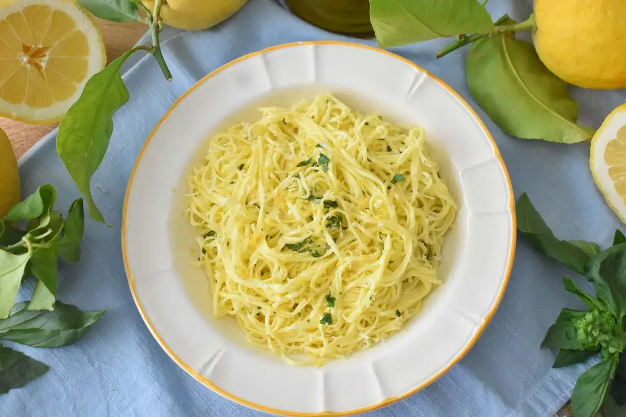 Pyszny makaron cytrynowy z ziołami i parmezanem, otoczony świeżymi cytrynami i bazylią.