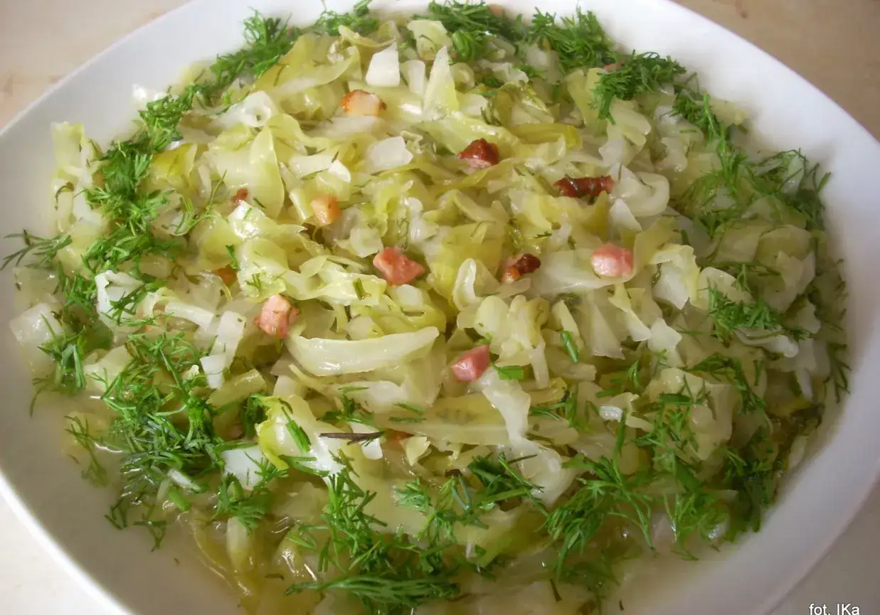 Młoda kapusta z koperkiem, przepis babci. Aromatyczne danie z dodatkiem skwarek, podane na białym talerzu.