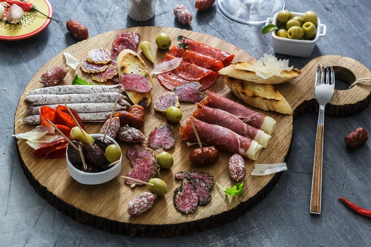 Deska wędlin: salami, prosciutto, oliwki, pieczywo. Zastanawiasz się chorizo co to? To pikantna, suszona kiełbasa, idealna na przekąskę.