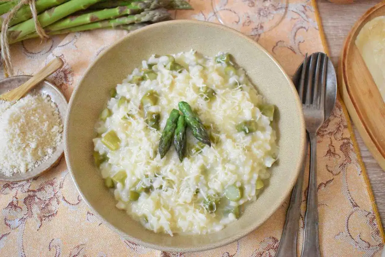 Kremowe risotto bianco z zielonymi szparagami i parmezanem, udekorowane pęczkami szparagów.