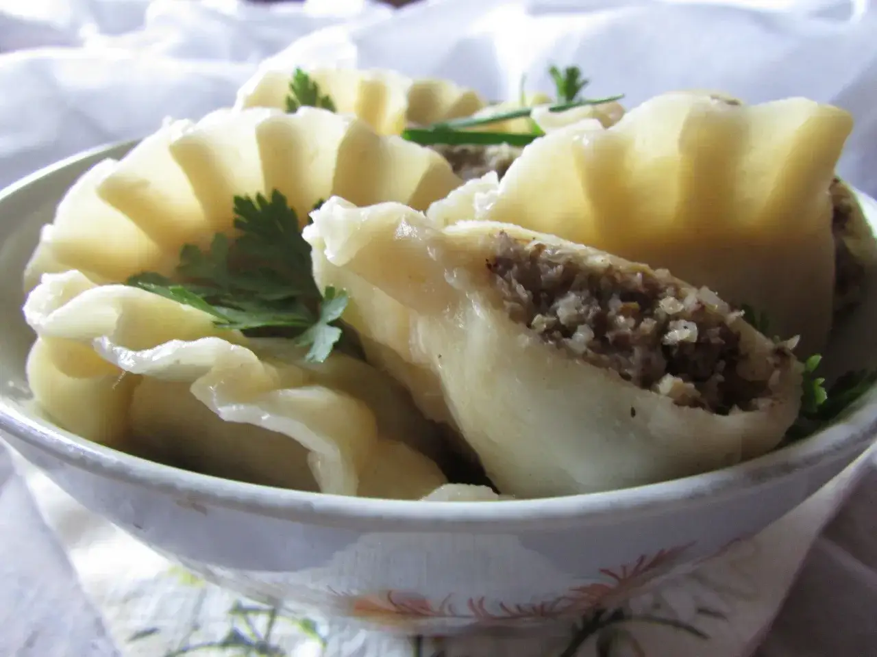 Pyszne pierogi z kaszą gryczaną i grzybami, udekorowane natką pietruszki, w misce.