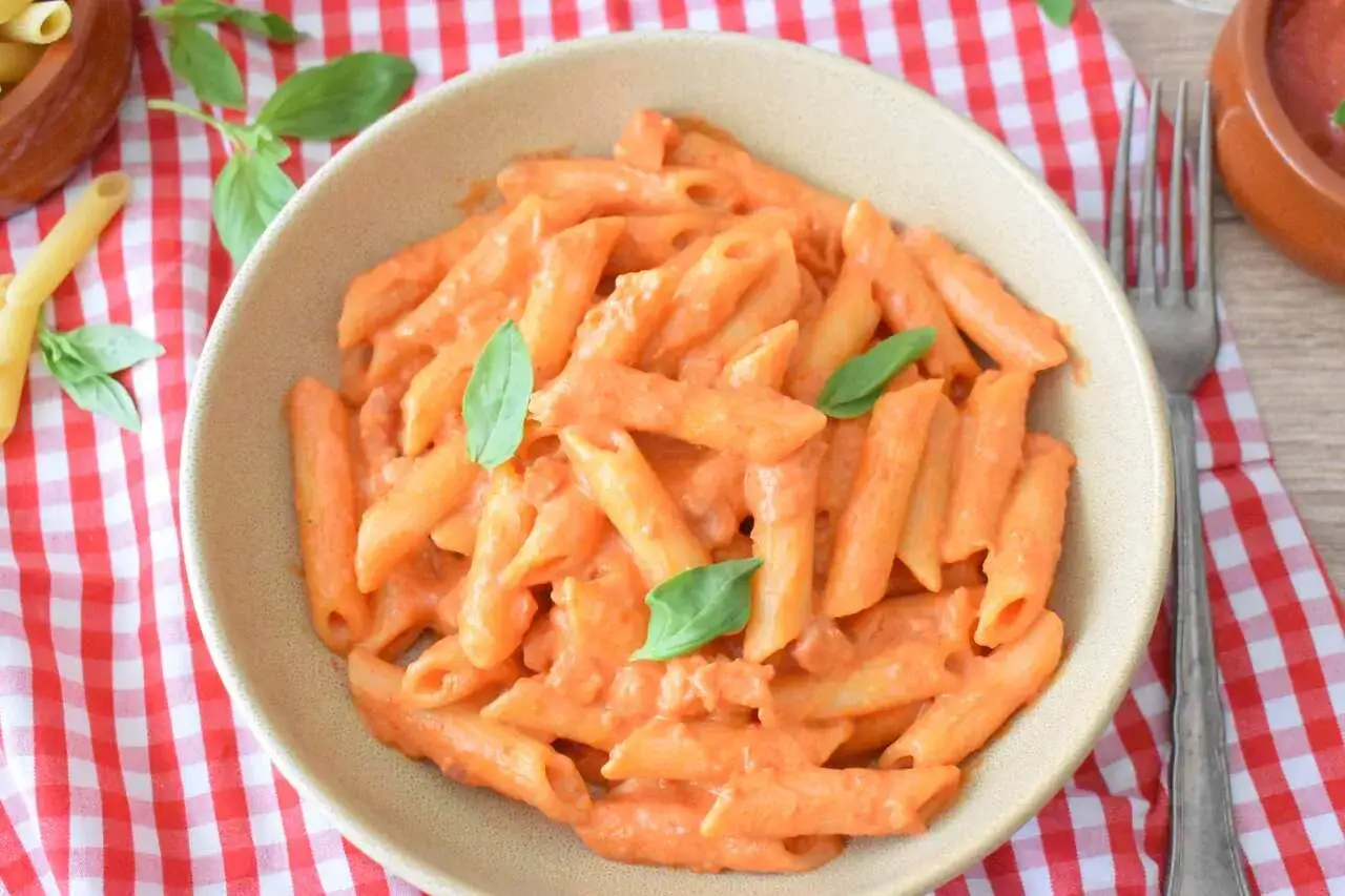 Penne z kremowym sosem pomidorowym i chrupiącą pancettą, udekorowane listkami bazylii. Pyszne danie makaronowe.