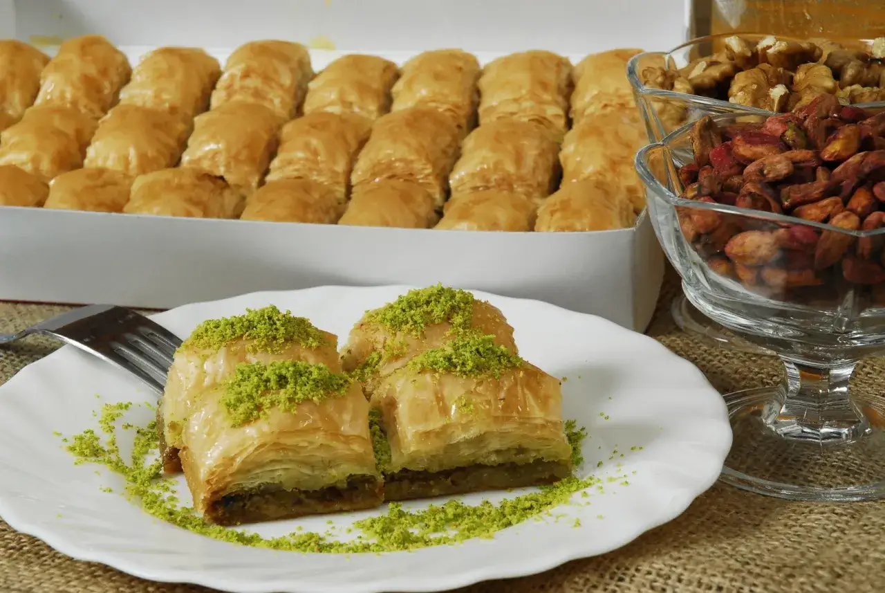 Pyszne słodycze z Cypru: baklava posypana pistacjami, obok orzechy i suszone owoce.