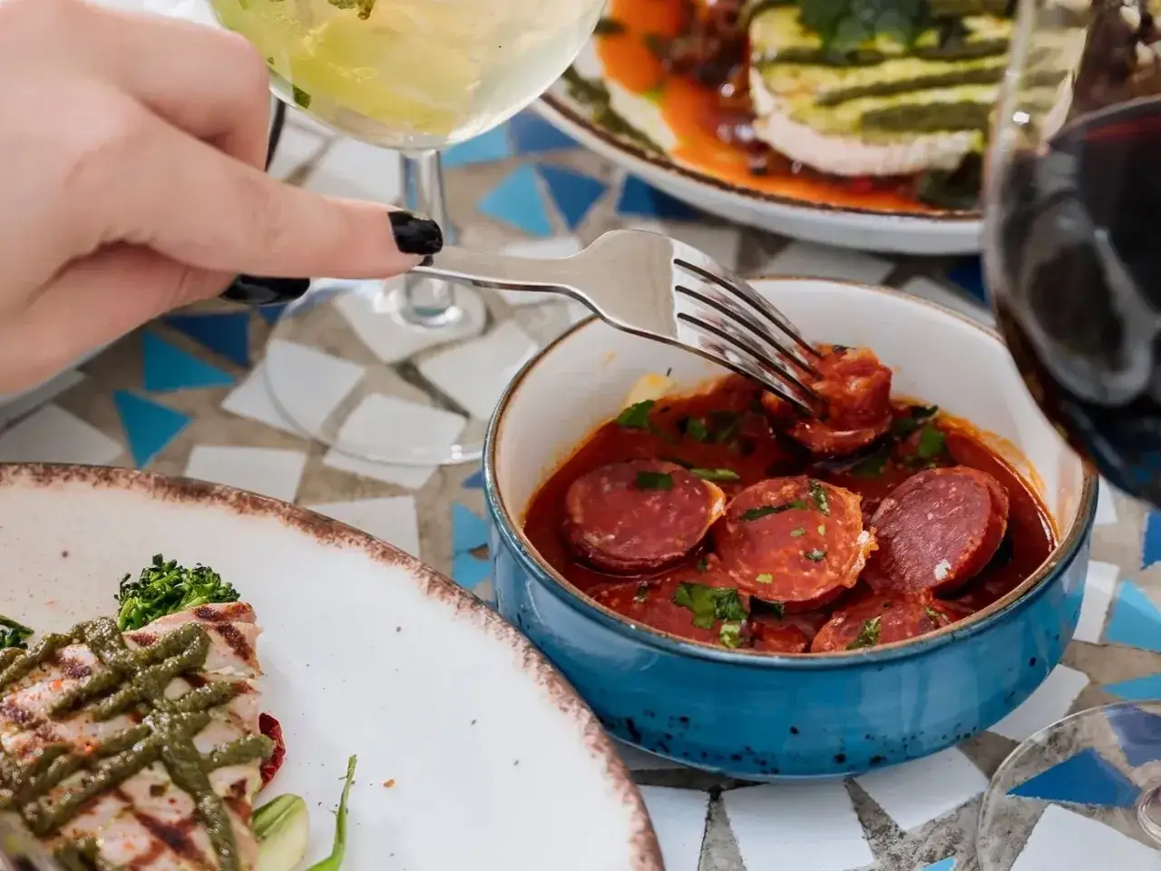 Widok z góry na talerz z grillowaną rybą i miseczkę z aromatycznym chorizo w cydrze, które jest nabierane widelcem.
