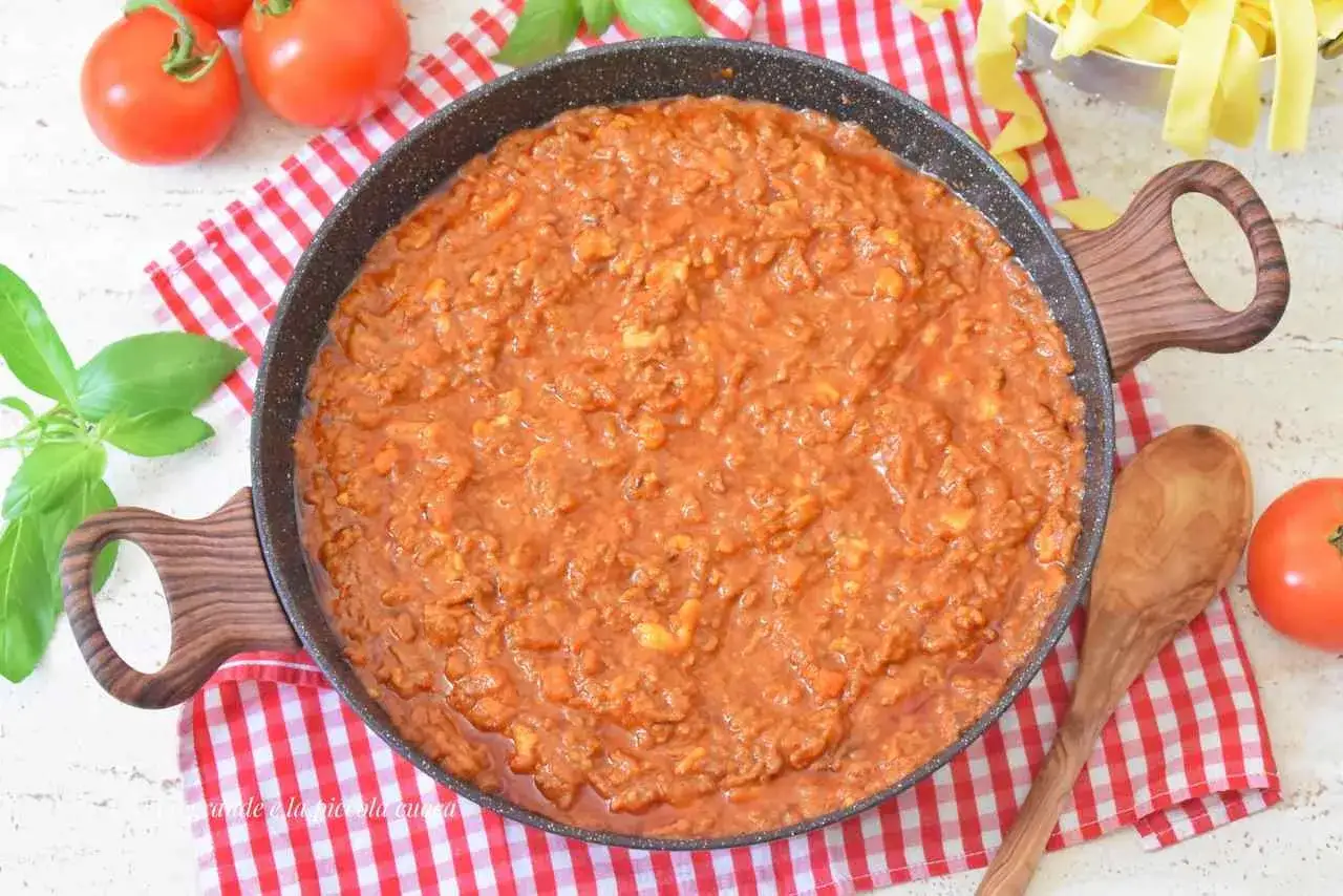 Gęsty sos bolognese z pomidorów w patelni, gotowy do podania ze spaghetti. Obok świeże pomidory i bazylia.