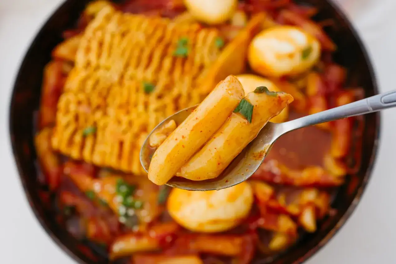 Łyżka pełna pysznych koreańskich noodle (tteokbokki) z jajkami i kawałkiem ciasta ryżowego.