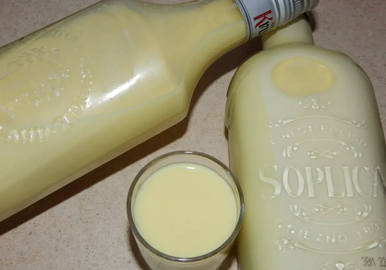 Kremowy likier, przypominający smakiem crema di limoncello, w szklance i butelkach Soplica.
