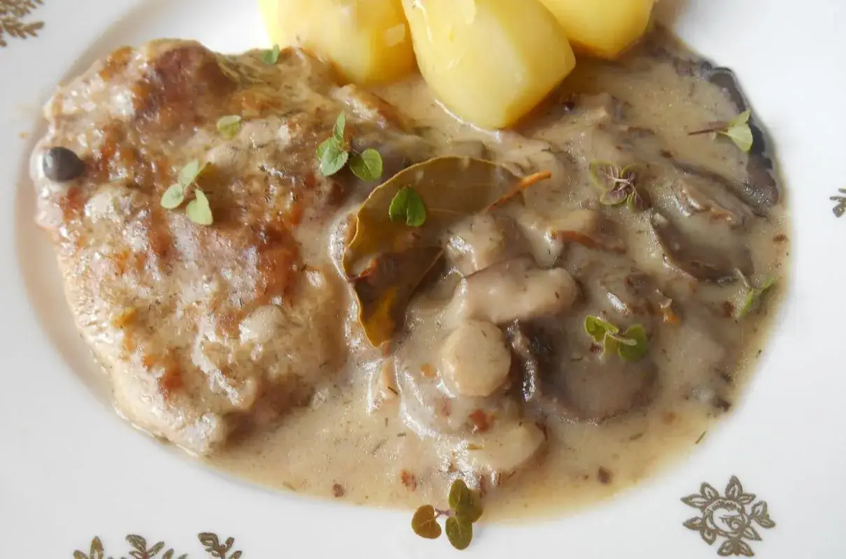 Pyszna karkówka w sosie grzybowym z ziemniakami, udekorowana listkami ziela angielskiego i świeżymi ziołami.