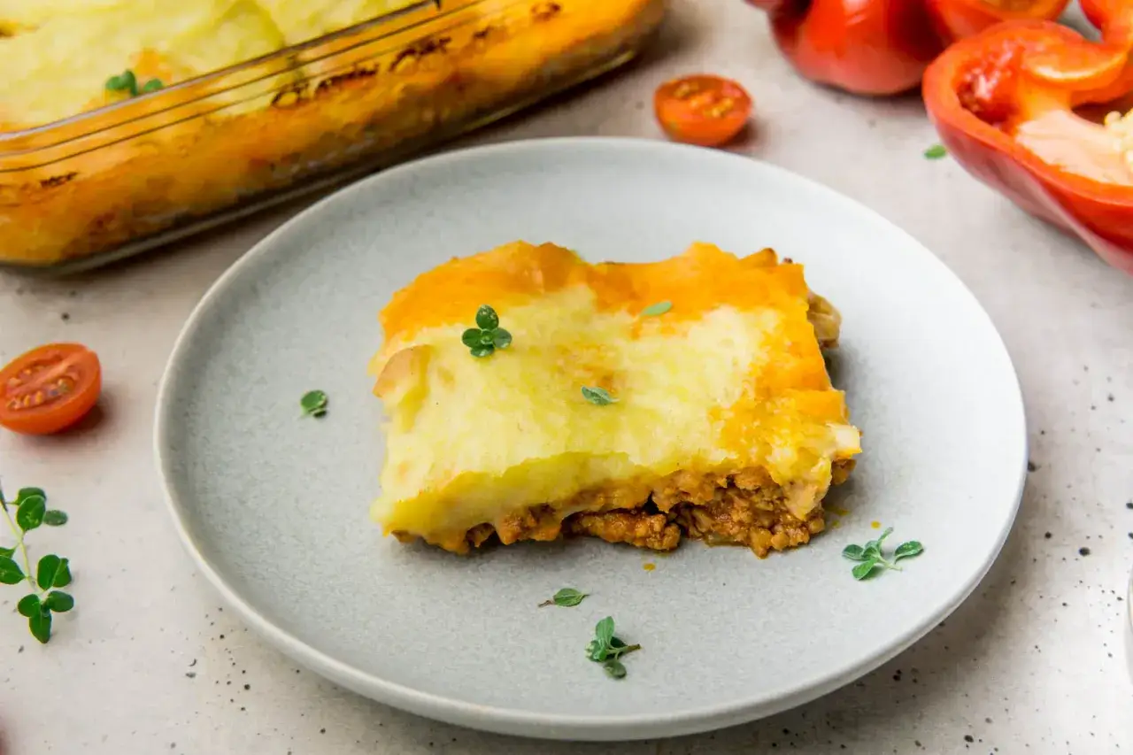 Pyszna zapiekanka pasterska z warstwą mięsa mielonego i kremowym purée ziemniaczanym, udekorowana świeżymi ziołami.