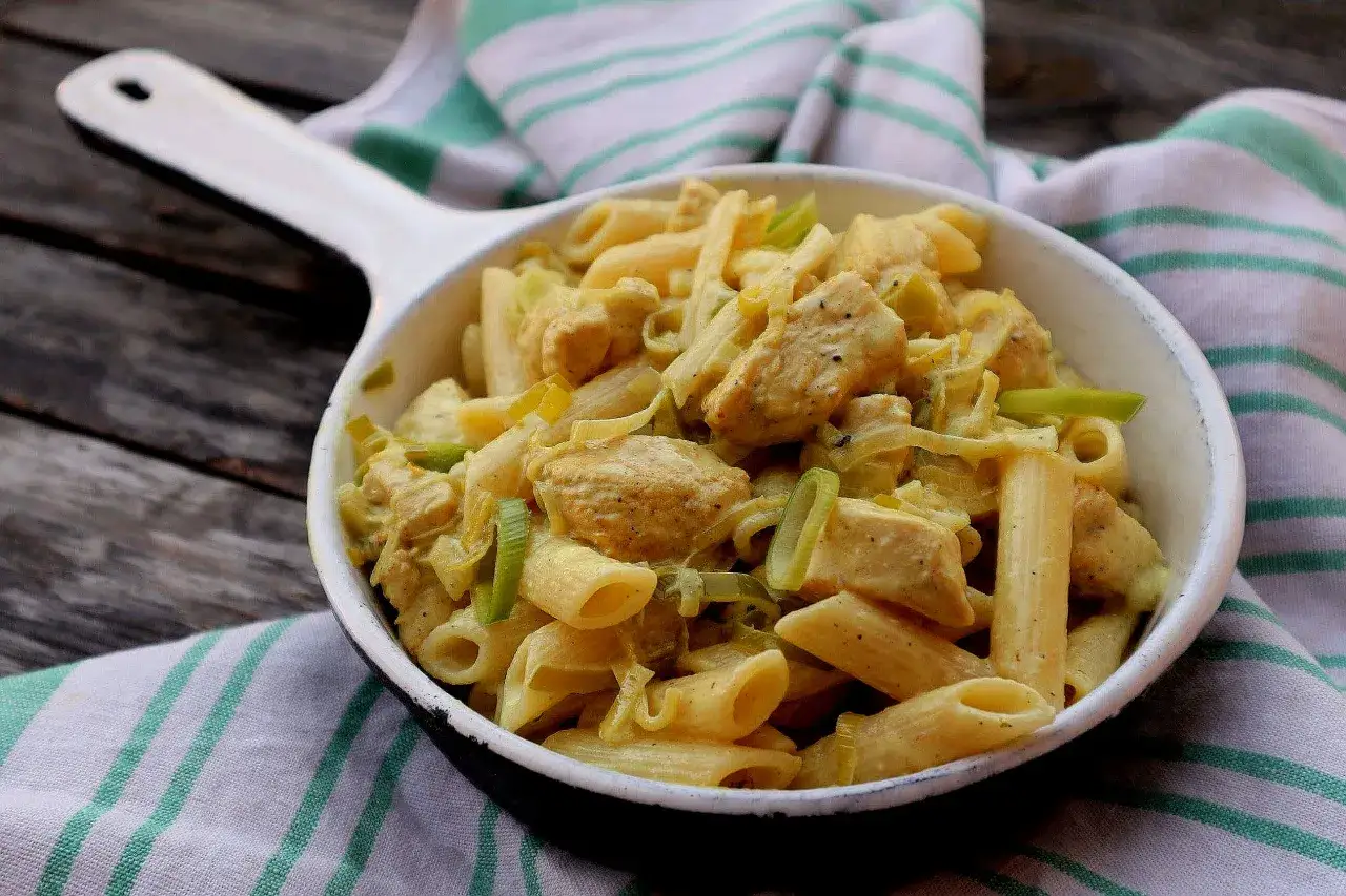 Penne z porem i kurczakiem w kremowym sosie, podane w białej misce na drewnianym stole.