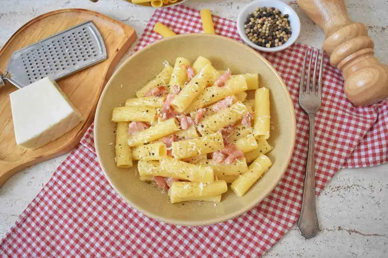 Pyszny makaron z pecorino, okraszony świeżo mielonym pieprzem. Obok kawałek sera i tarka.