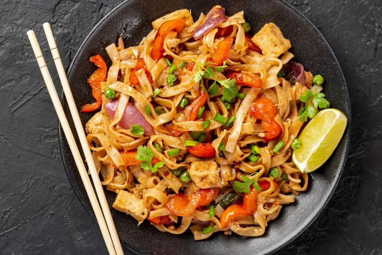 Pyszny pad thai makaron z tofu, warzywami i limonką, gotowy do jedzenia pałeczkami.