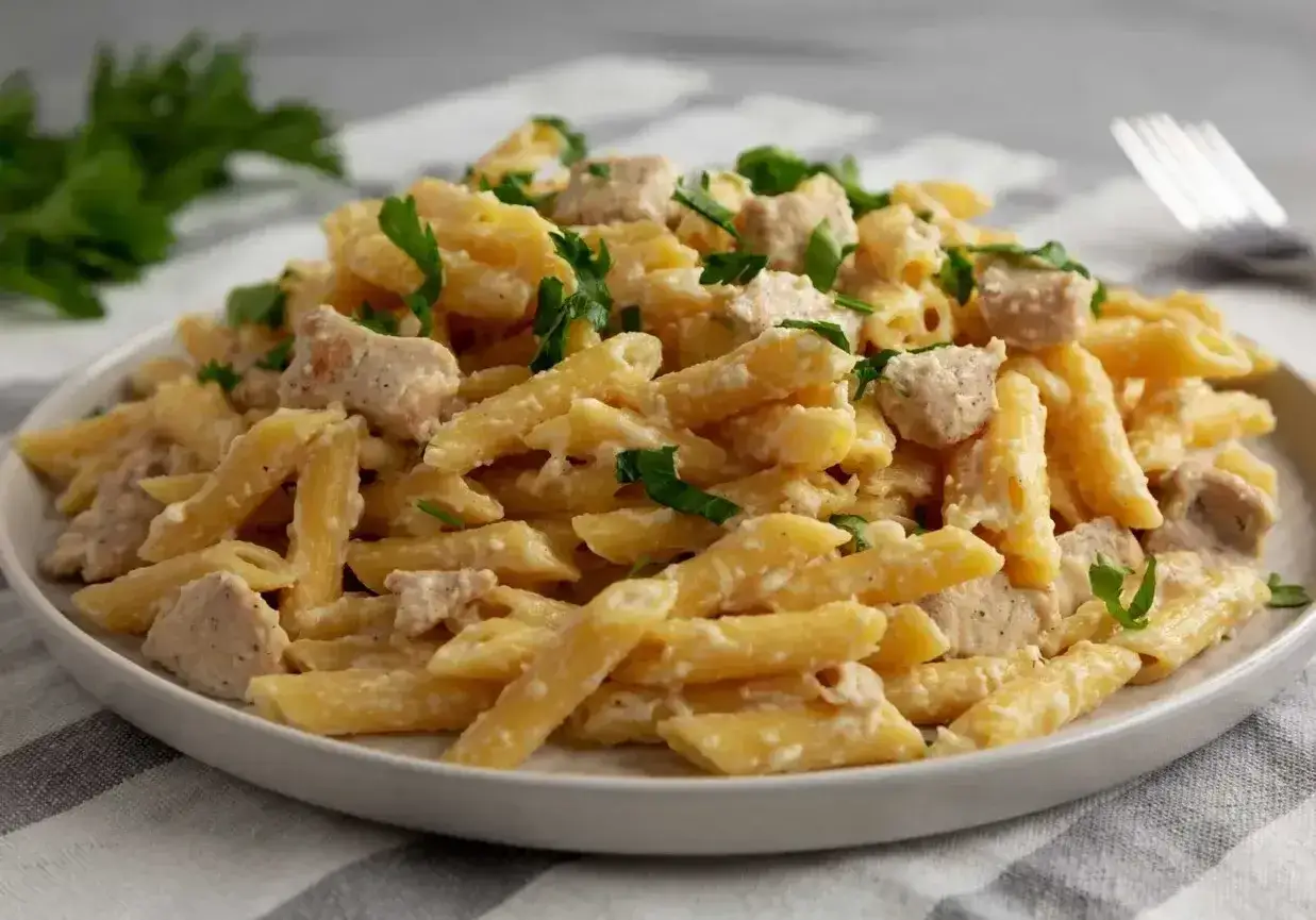 Penne po włosku z kawałkami kurczaka w kremowym sosie, posypane świeżą natką pietruszki.