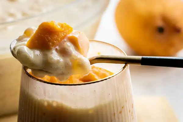 Słodkie monoporcje mango z kremowym deserem, podane w szklance. Obok leży dojrzałe mango.