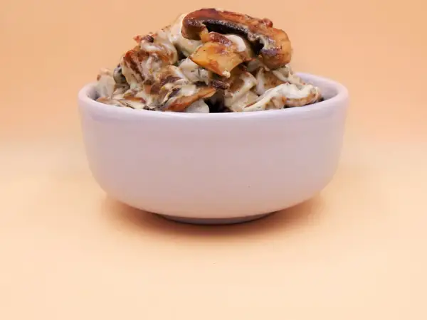Tofu z pieczarkami w kremowym sosie, podane w białej miseczce.