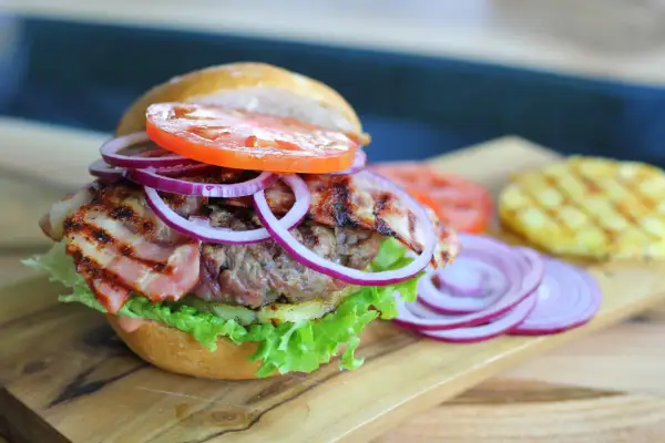Pyszny, małomiasteczkowy burger z soczystą wołowiną, chrupiącym boczkiem, świeżą sałatą, pomidorem i czerwoną cebulą.