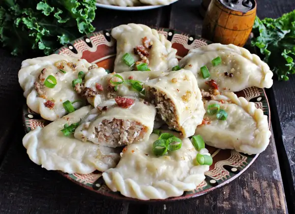 Pyszne pierogi z kaszą gryczaną i serem białym, okraszone skwarkami i szczypiorkiem, na ozdobnym talerzu.