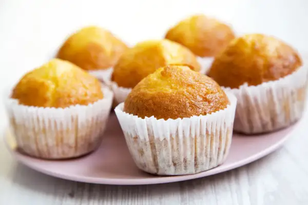 Kilka apetycznych, zdrowe muffinki w papierowych foremkach na różowym talerzu.