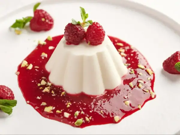 Panna cotta przepis: aksamitny deser z malinowym sosem, pistacjami i świeżymi malinami. Idealny na letnie popołudnie.