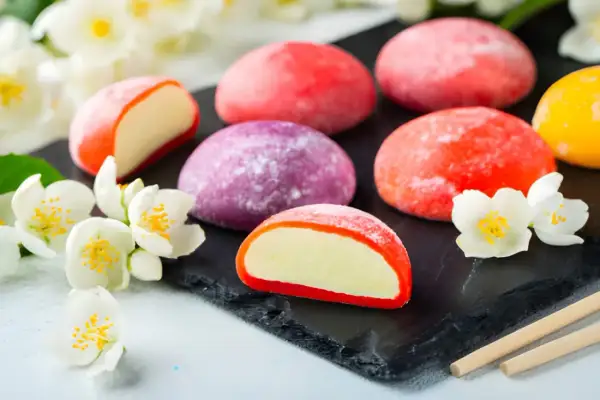 Kolorowe japońskie desery mochi, otoczone białymi kwiatami jaśminu, kuszą swoim wyglądem i smakiem.