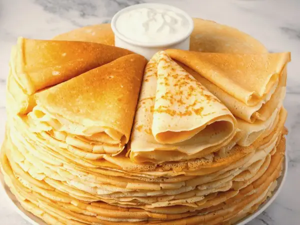 Stos puszystych naleśników z mąką ziemniaczaną, ułożonych w wachlarz wokół miseczki ze śmietaną.