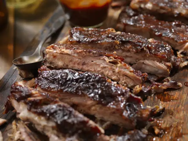 Soczyste żeberka w piwie, polane gęstym sosem BBQ, prezentują się apetycznie na drewnianej desce.