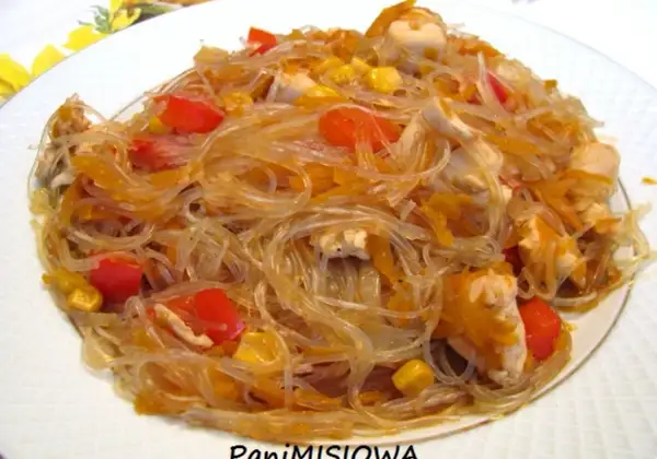 Pyszny kurczak z makaronem sojowym, papryką i kukurydzą na białym talerzu.