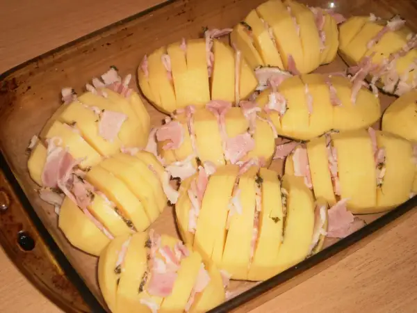 Ziemniaki hasselback z boczkiem i serem, gotowe do pieczenia w naczyniu żaroodpornym.