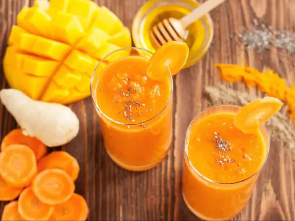 Dwa szklanki pomarańczowego koktajlu z mango i marchewki, ozdobione plasterkiem marchewki i nasionami chia.