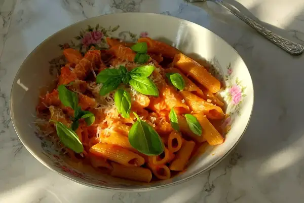 Penne arrabiata z bazylią i parmezanem, podane w ozdobnej misce.