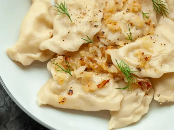 Pyszne pierogi z ziemniakami, okraszone cebulką i koperkiem, posypane pieprzem.
