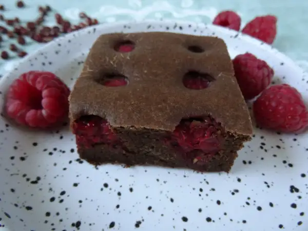 Pyszny fit brownie z fasoli, z malinami w środku i na talerzu. Idealny deser dla łasuchów.