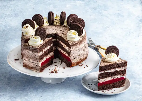 Pyszny tort oreo z kremem, malinową warstwą i ciasteczkami oreo na wierzchu. Kawałek ciasta na talerzyku.