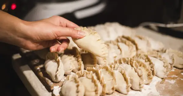 Dłoń trzyma surowe pierogi, gotowe do wrzucenia do gotującej wody.
