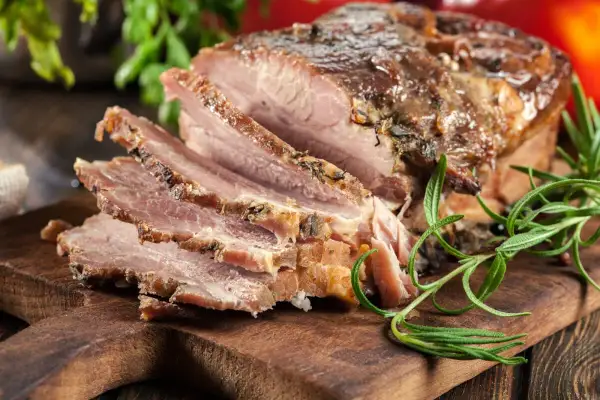 Pokrojony, pieczony boczek z ziołami na desce. Idealny przykład, jak zapeklować boczek do pieczenia, by był soczysty i aromatyczny.