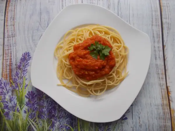 Spaghetti ze świeżych pomidorów, udekorowane natką pietruszki, na białym talerzu, na tle drewnianego blatu i lawendy.