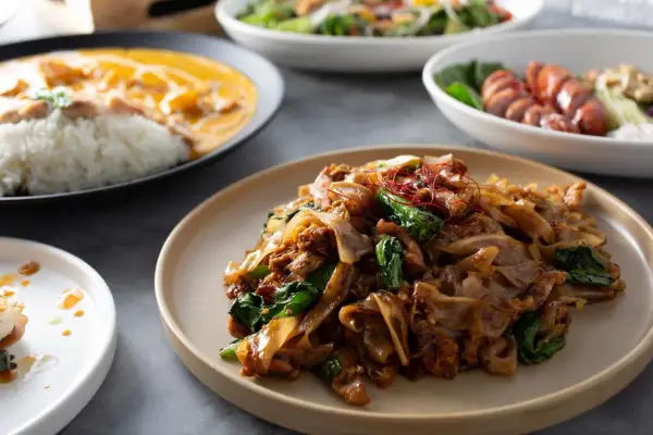 Pyszny pad thai makaron z kurczakiem i warzywami, podany na talerzu. Obok widać inne dania.