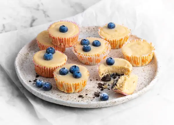 Pyszne serniczki Oreo z jagodami na talerzu. Jeden serniczek jest przekrojony, ukazując kremowe wnętrze i ciemny spód.