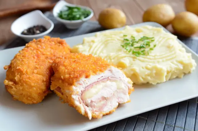 Chrupiący kotlet szwajcarski z rozpływającym się serem i szynką, podany z kremowym purée ziemniaczanym.